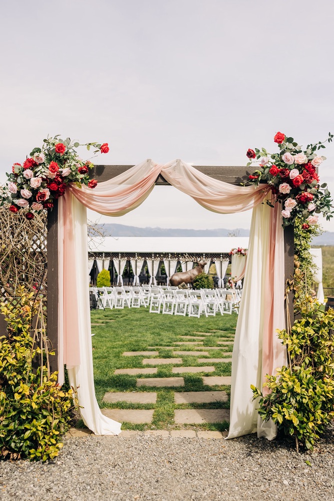 Garden arch at Eagle Mountain Venue dressed in blush drapery and red and pink silk florals to match the Mandap