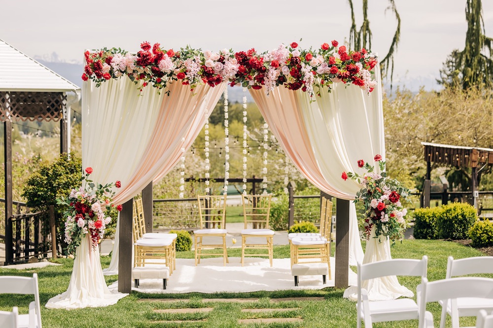 Four-post Hindu wedding Mandap with blush and ivory drapery, red and pink silk floral canopy and gold seating at Eagle Mountain Venue in Arlington