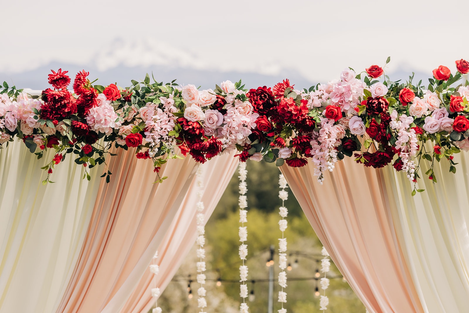Red and pink silk floral canopy across a blush and ivory Mandap, with jasmine garlands and a mountain view, at Eagle Mountain Venue in Arlington