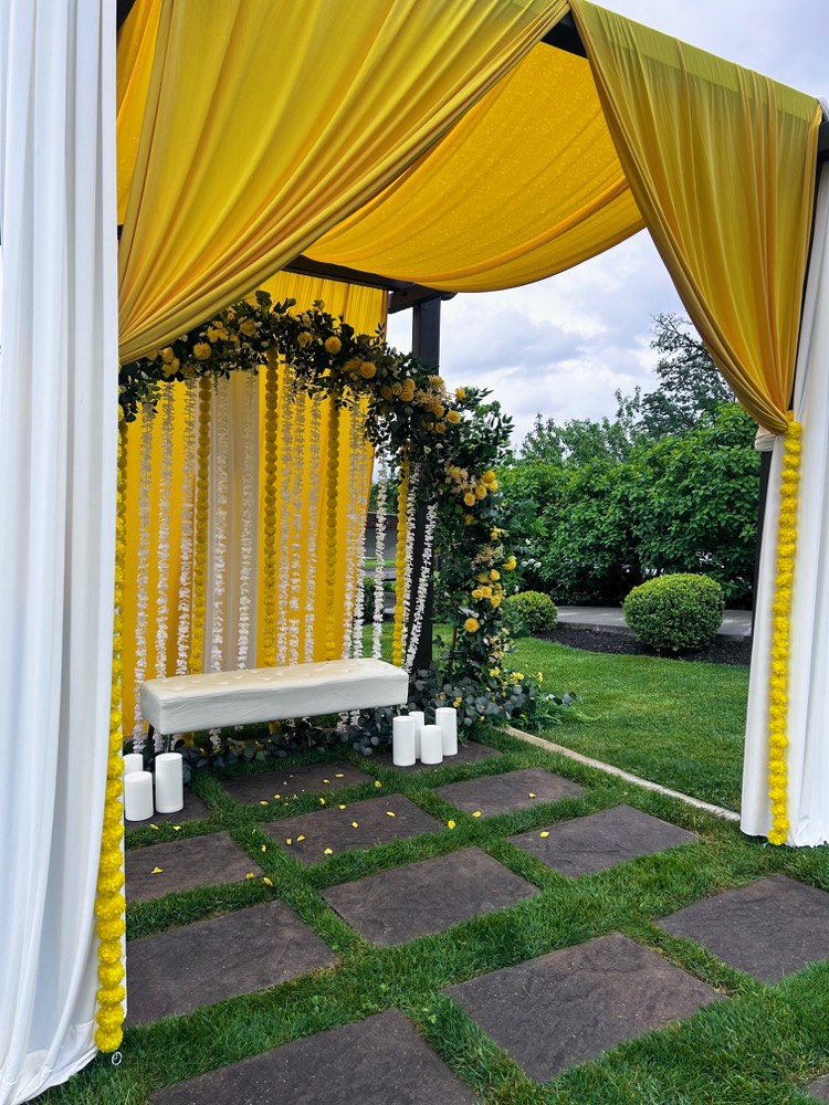 Side view of haldi decor with yellow and white drapery, marigold garlands and a tufted bench at Eagle Mountain Venue