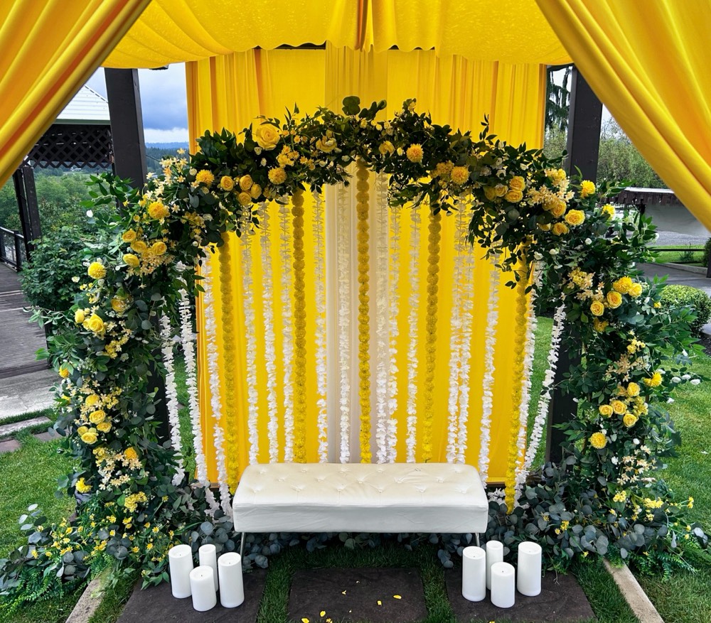 Haldi decor with yellow drapery, a yellow floral arch, marigold garlands and a white tufted bench at Eagle Mountain Venue