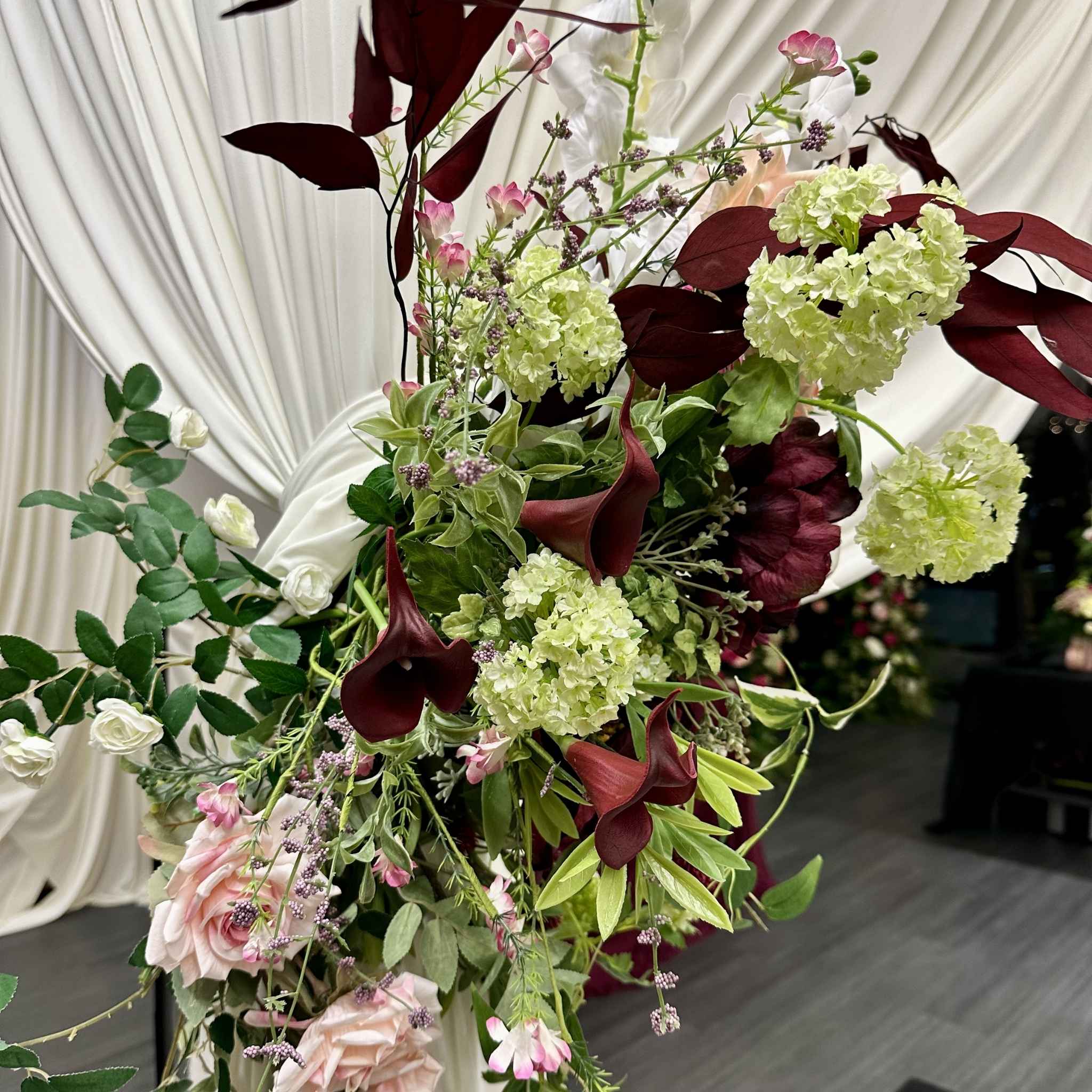 Close-up of a burgundy faux floral arrangement with roses and hydrangeas, attached to a Manadao Structure, designed by Bradbury Events
